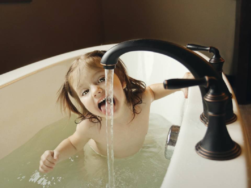 Girl in Bathtub Tasting Water From Black Faucet